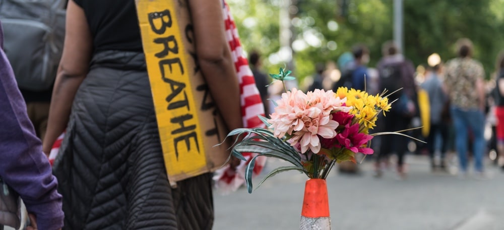 Person holding a can't breathe sign during the protests in 2020 in Seattle. Flowers in a caution cone and people in the background