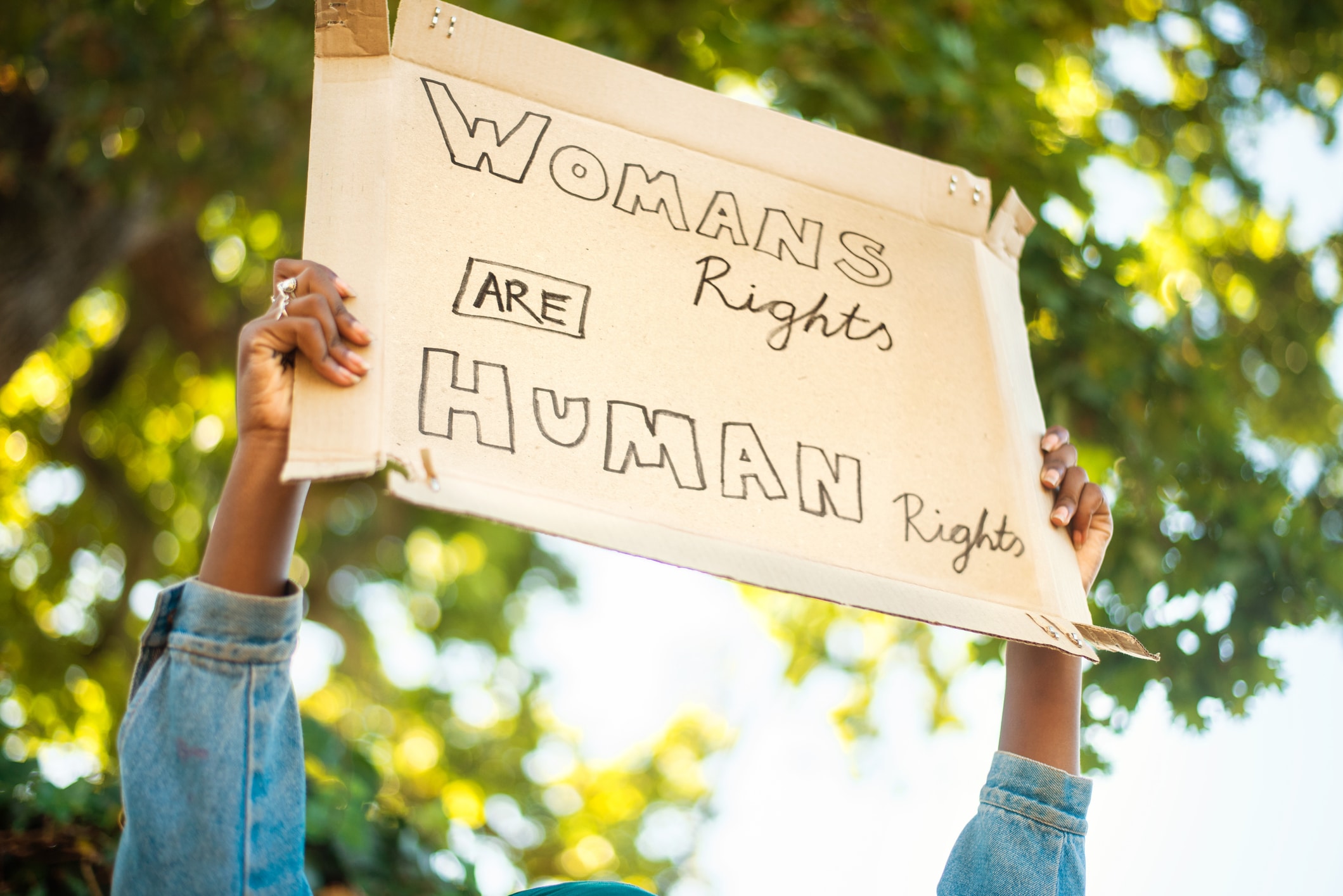 Close-up of an unrecognizable young African woman standing outside holding up a women's rights protest sign