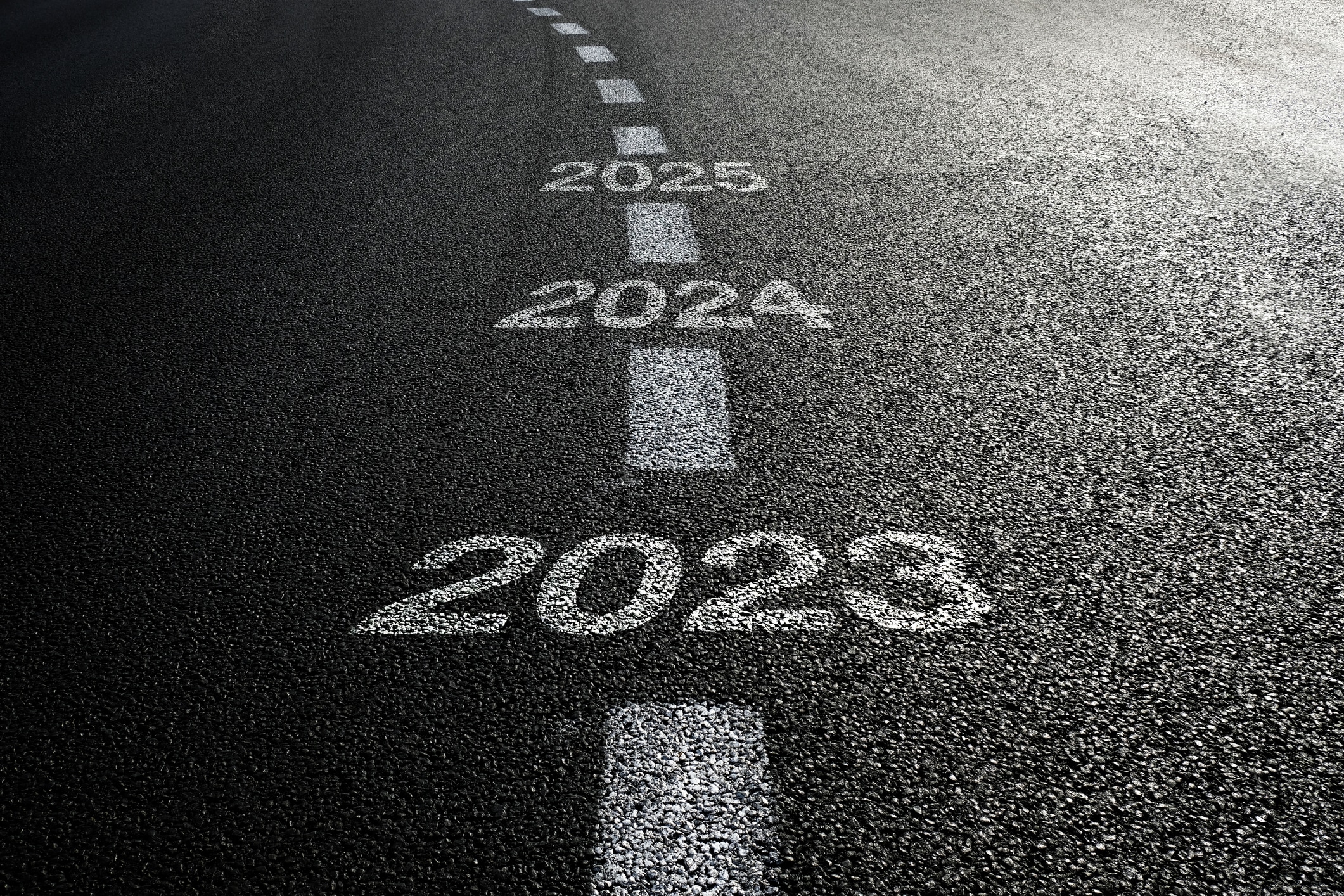 Road with white dashed lines and the numbers 2023, 2024, and 2025 written along the line.